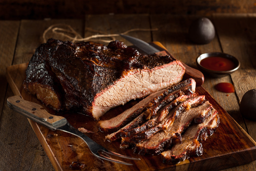 Sliced Brisket on cutting board with fork and barbeque sauce