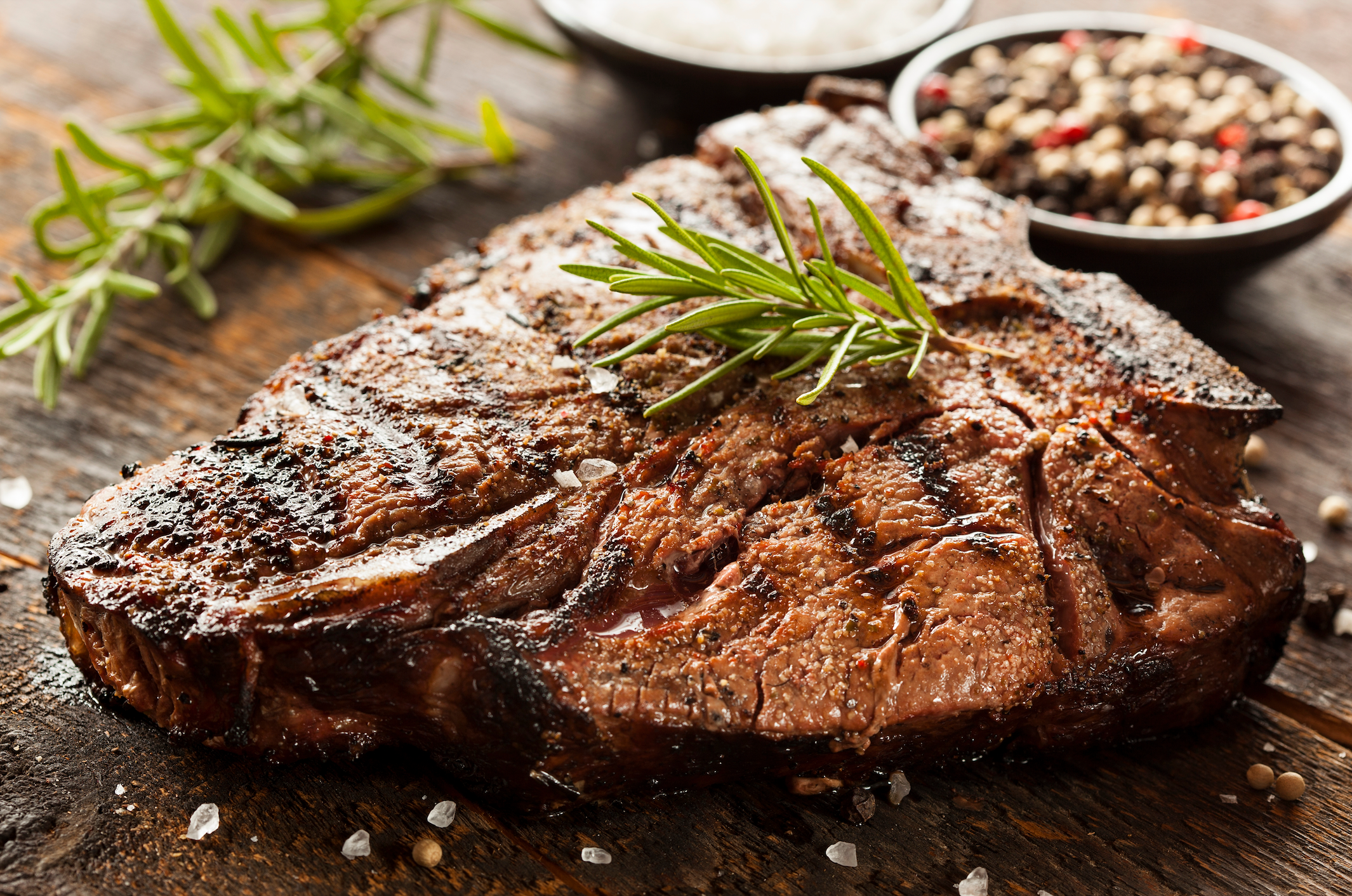 Grilled Ribeye steak on a cutting board with peppercorn and rosemary sprigs in the background